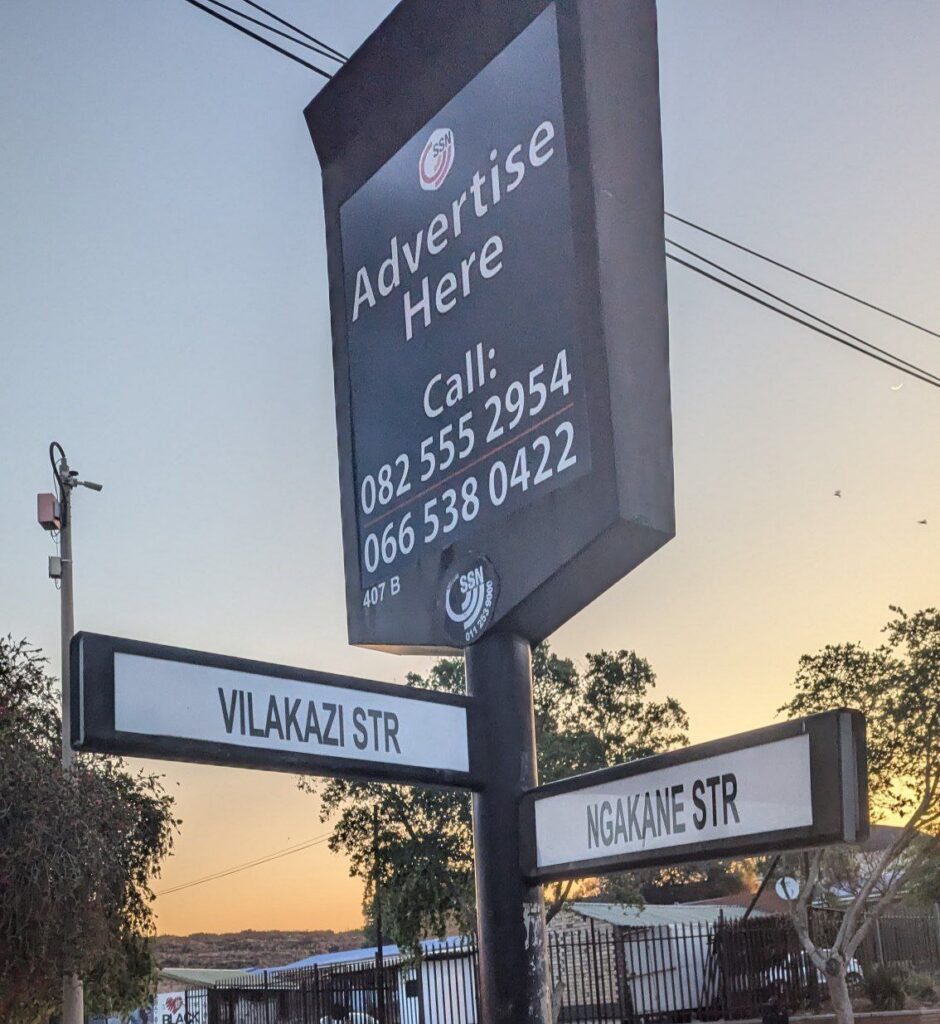 Street signs for Vilakazi Street and Ngakane Street beneath an advertising board in Soweto.